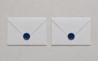 Two identical sealed envelopes lying side by side on a pale stone surface, each closed with the same unmarked navy wax seal, indistinguishable from one another